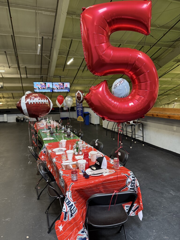 Red number five balloon with baseball and football decorations above a custom party table at BVSA